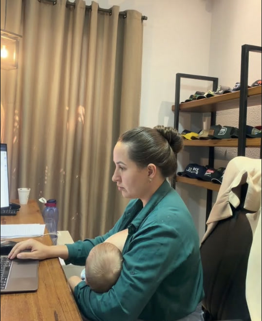 Ana trabalhando no notebook com o filho recém-nascido no colo